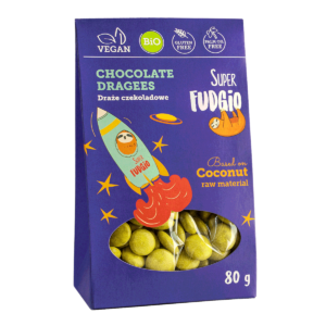 Ekologiczne wegańskie draże czekoladowe super fudgio; fioletowy kartonik z grafiką rakiety i leniwca lecącego w kosmos. Kanonik z okienkiem, widać zawartość - czekoladowe draże z kurkumą w kolorze żółtym