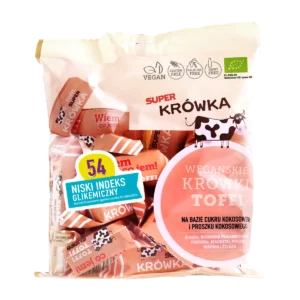 Ekologiczne wegańskie krówki bezmleczne o smaku toffi; foliowe kremowe opakowane z krówkami w papierku koloru łososiowego, przezroczyste okienko przez które widać zawartość, logo super krówka, po lewej stronie opakowania żółto-niebieska naklejka Niski Indeks glikemiczny.